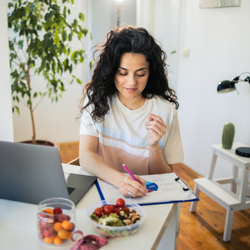 Woman with laptop at a table taking notes during online personalised wellbeing consultation sesson